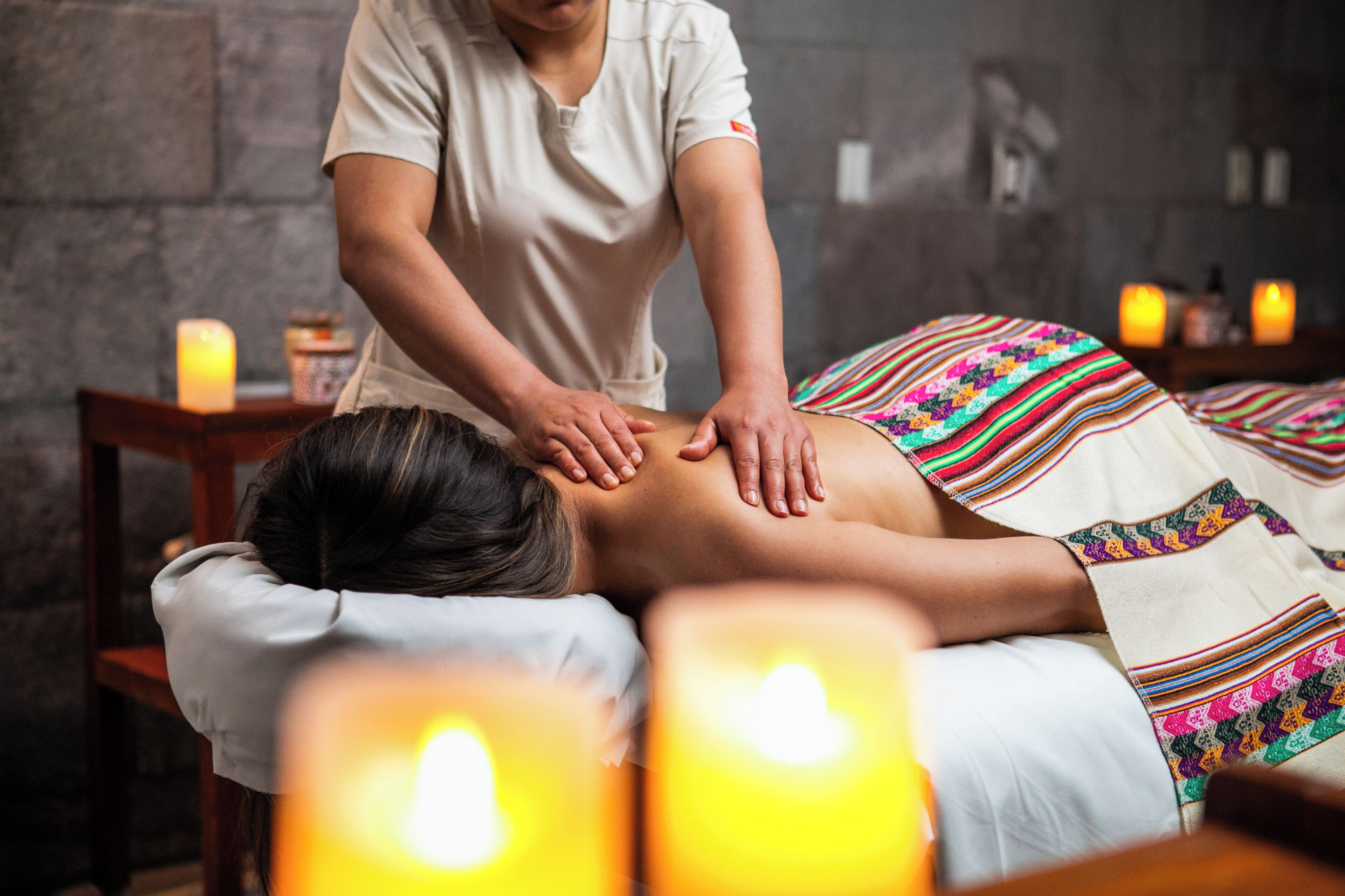 Sessão de massagem em um quarto com velas e parede de pedra.