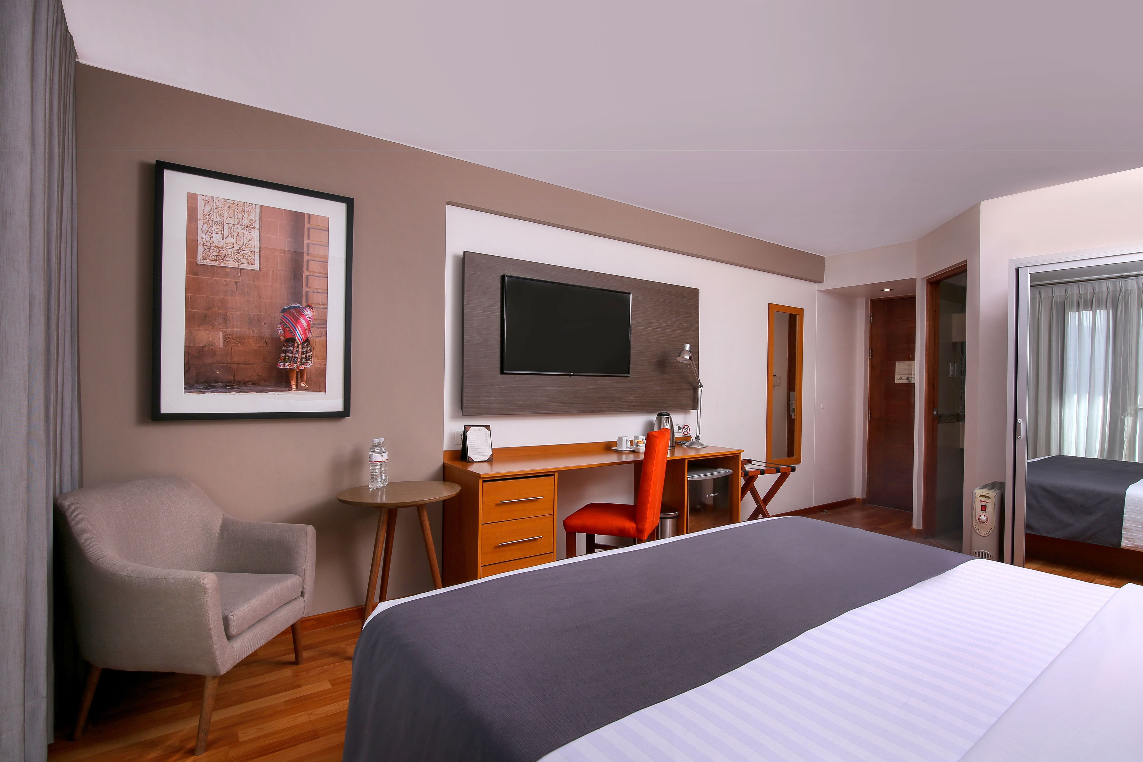 A hotel room with a bed, a desk with a chair, a television, and a framed picture on the wall.