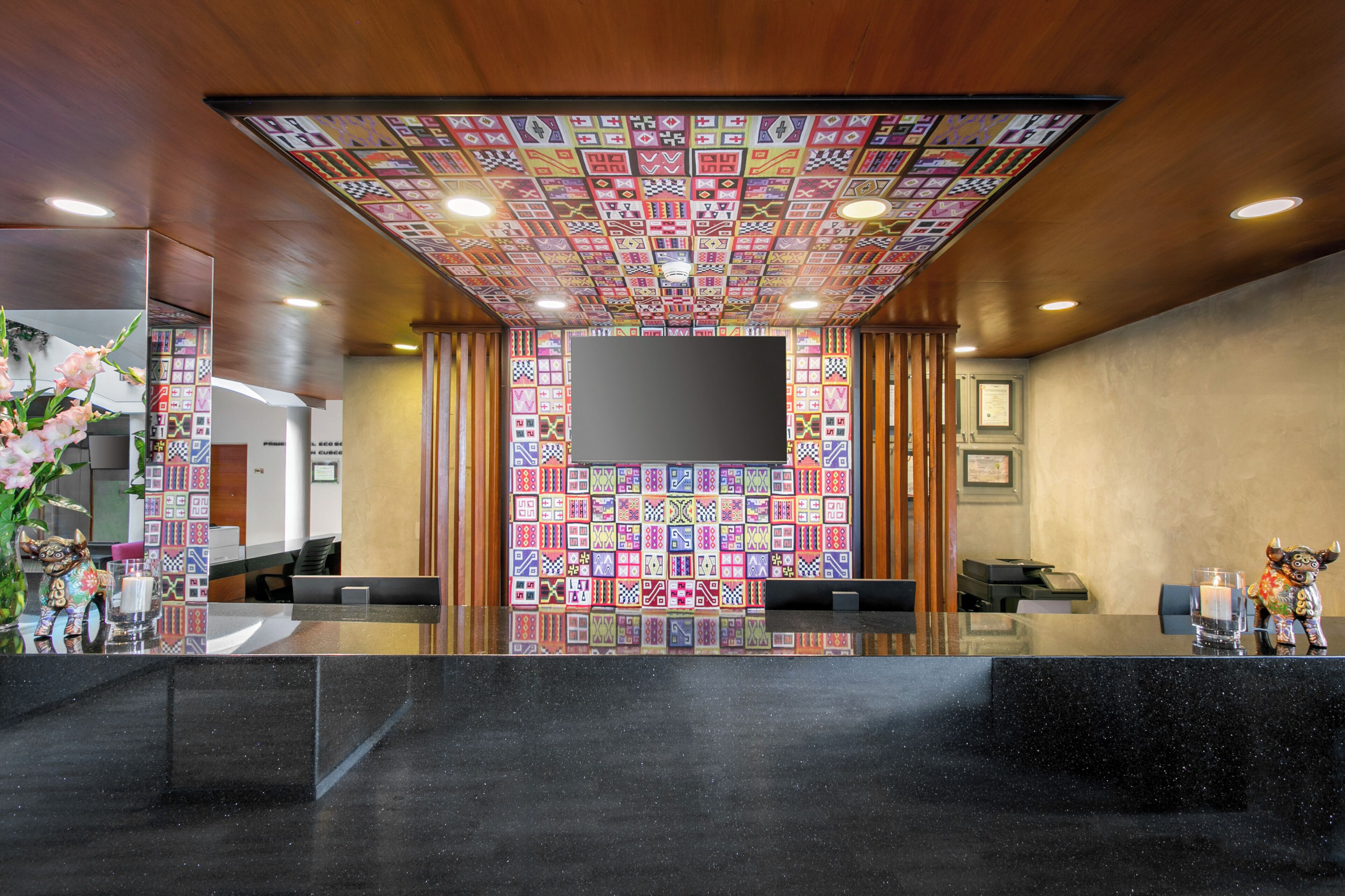 A reception area with a black reception desk, a flat-screen TV mounted on the wall, and a colorful patterned ceiling.