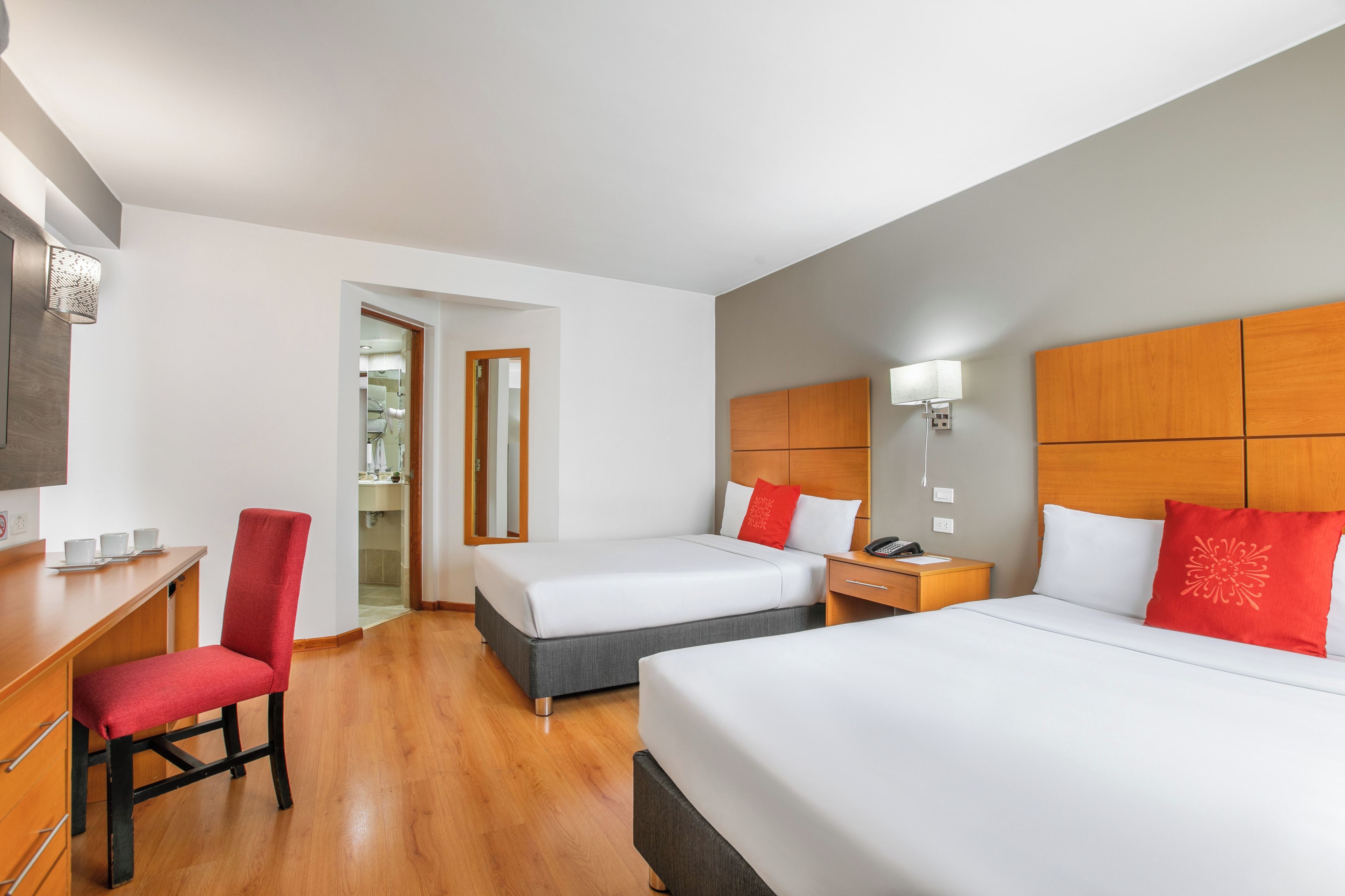 Camera d'albergo con due letti, una scrivania, una sedia e bagno visibile tramite una porta aperta.
