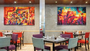 Un comedor con mesas y sillas, dos grandes cuadros abstractos en las paredes y un techo de madera.