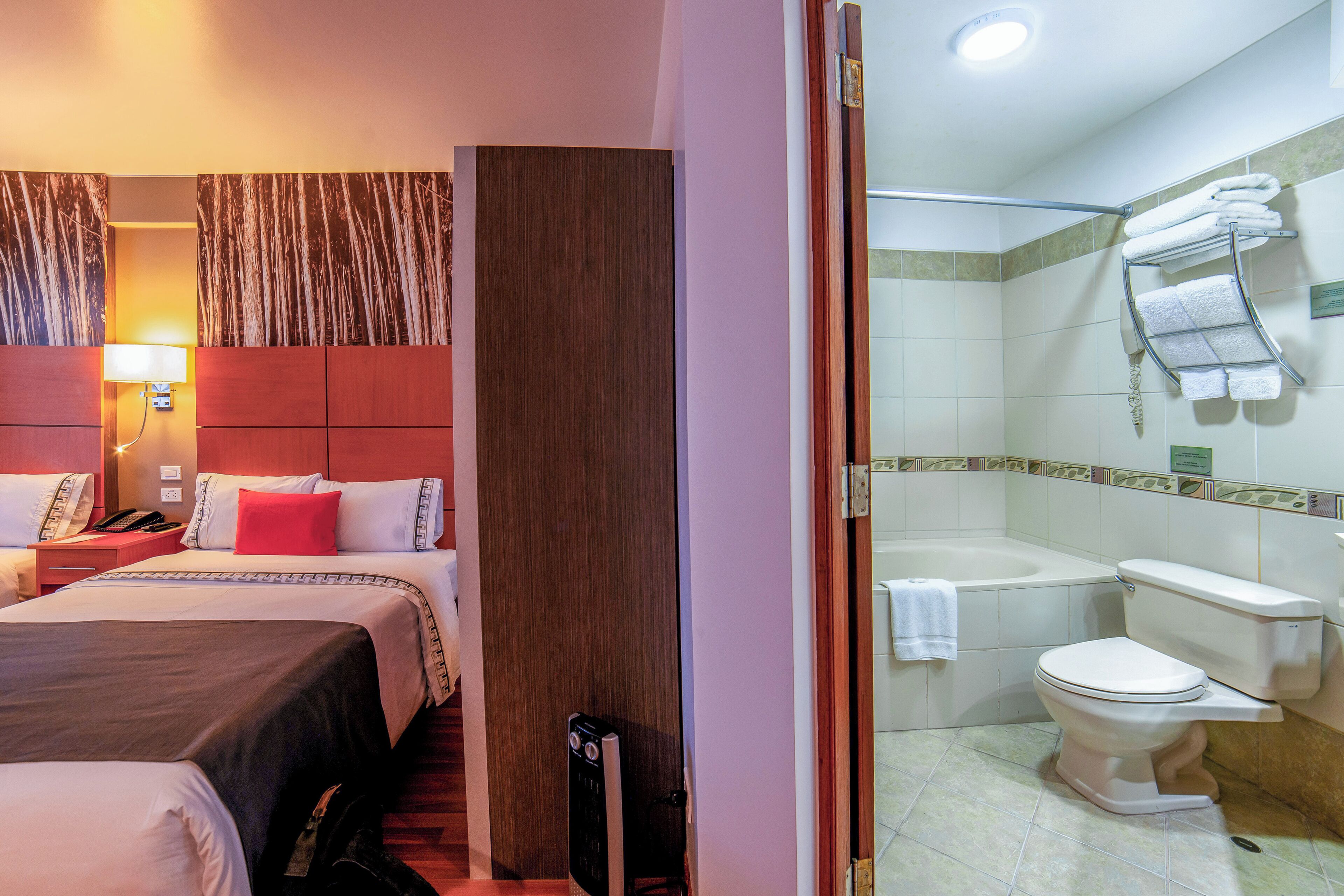 Una habitación de hotel con una cama, una mesita de noche con lámpara, un teléfono y una almohada roja.