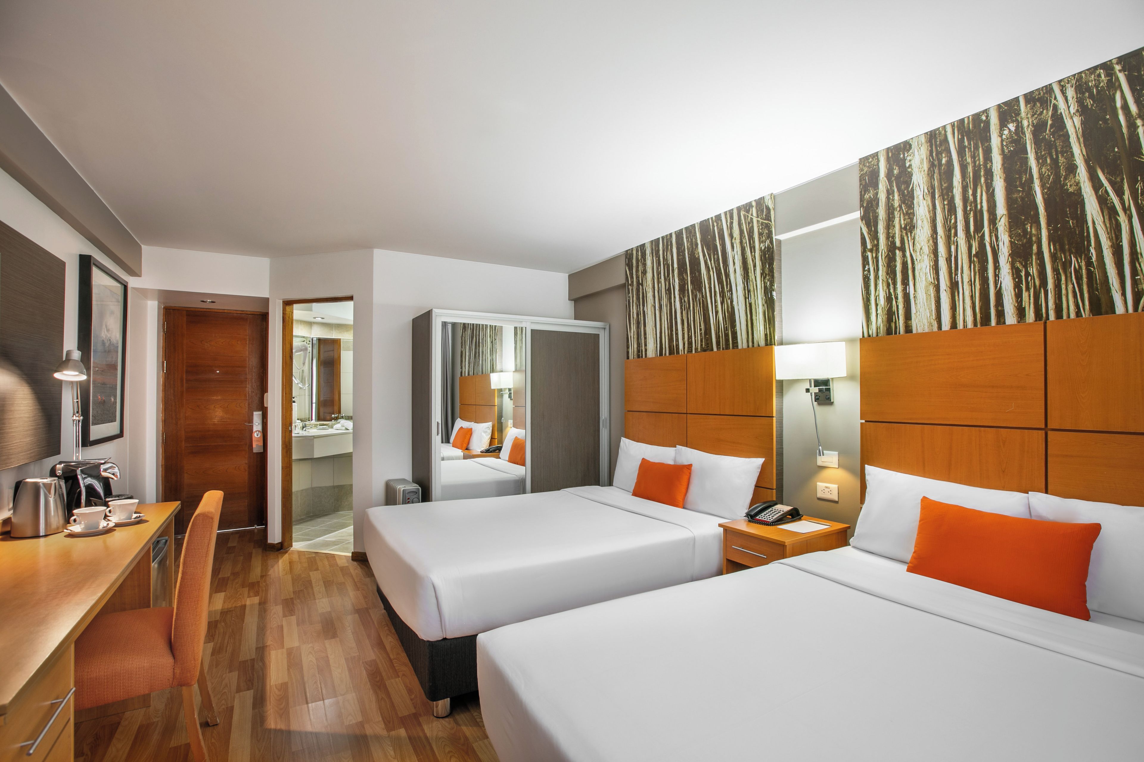 Habitación de hotel con dos camas, un escritorio, una silla, una cafetera y un espejo.