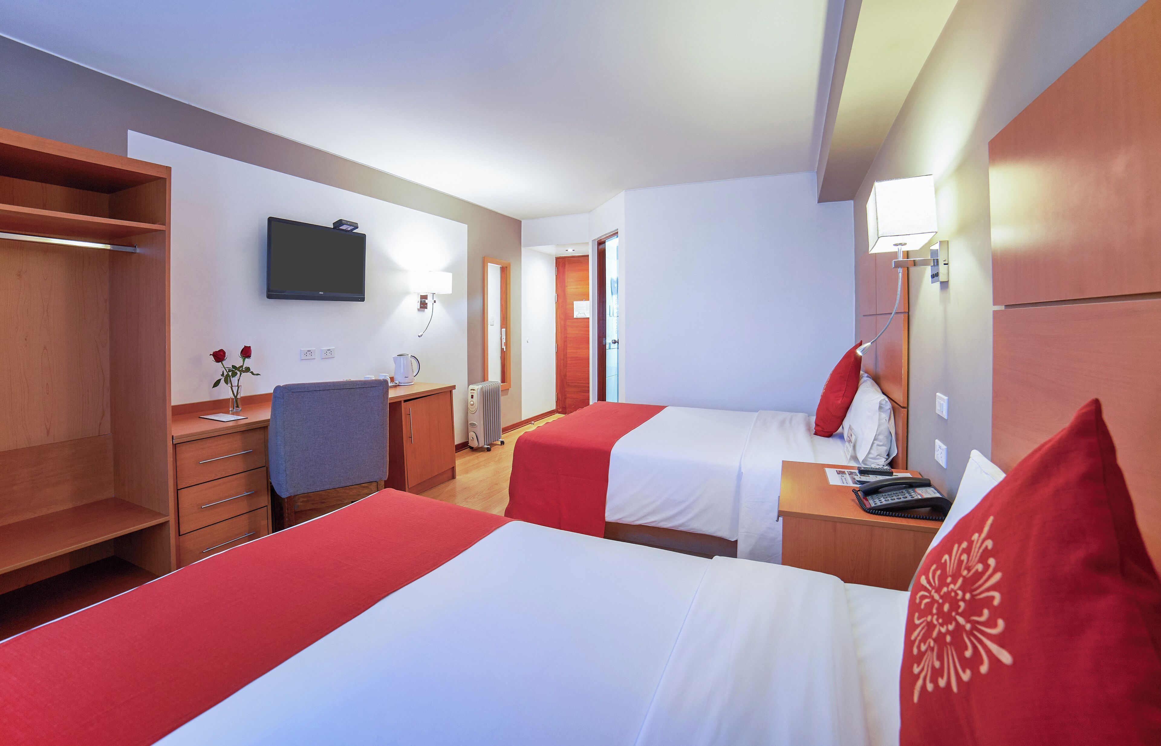 Habitación de hotel con dos camas, un escritorio, una silla, un televisor y una mesita de noche con lámpara.