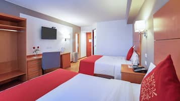 Habitación de hotel con dos camas, un escritorio, una silla, un televisor y una mesita de noche con lámpara.