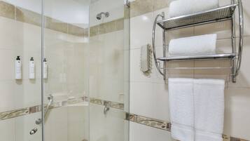 A glass-enclosed shower with a chrome towel rack holding two towels, and a wall-mounted soap dispenser.