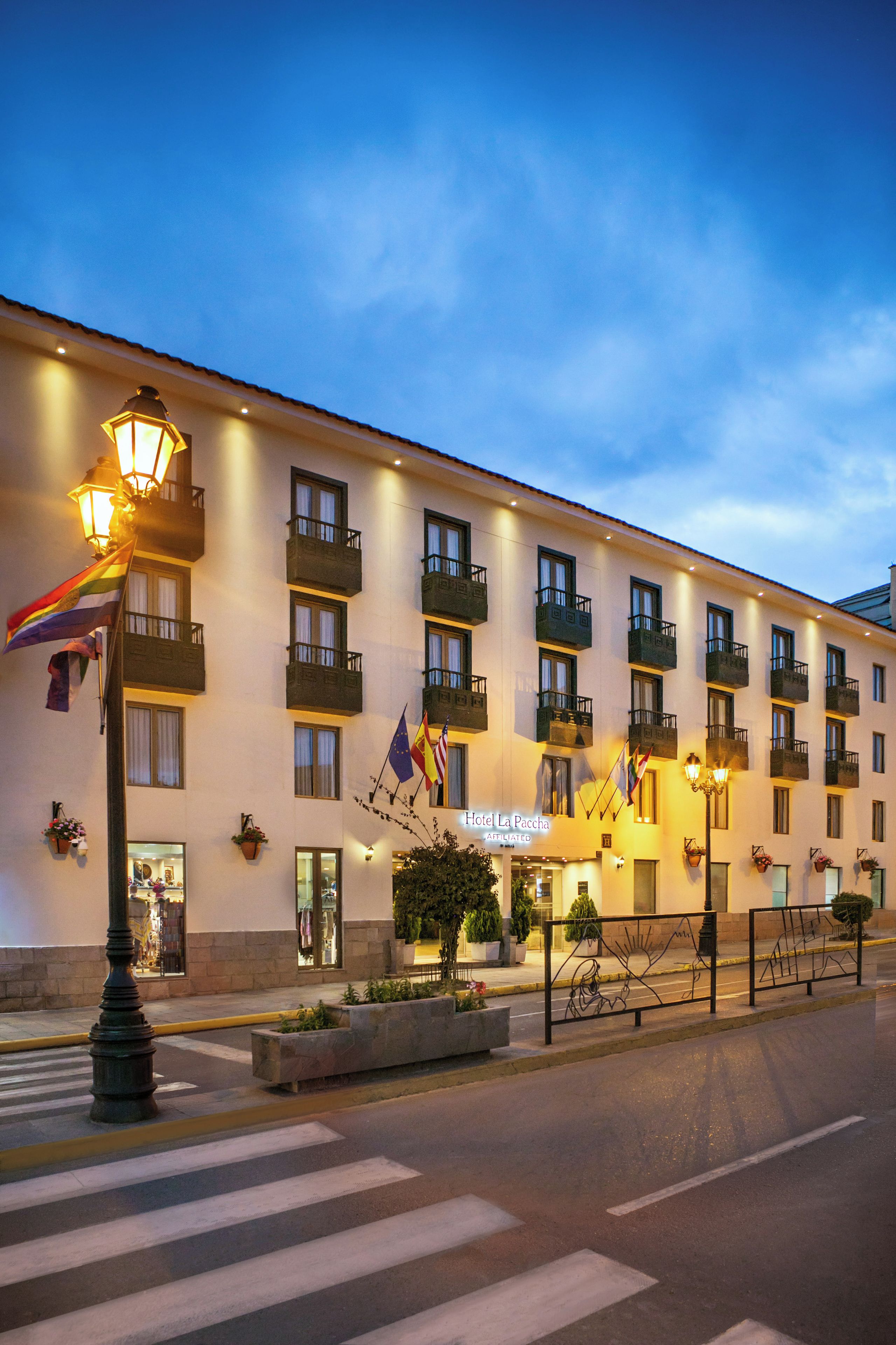 Un hotel con varios balcones, una entrada bien iluminada y un paso de peatones enfrente.