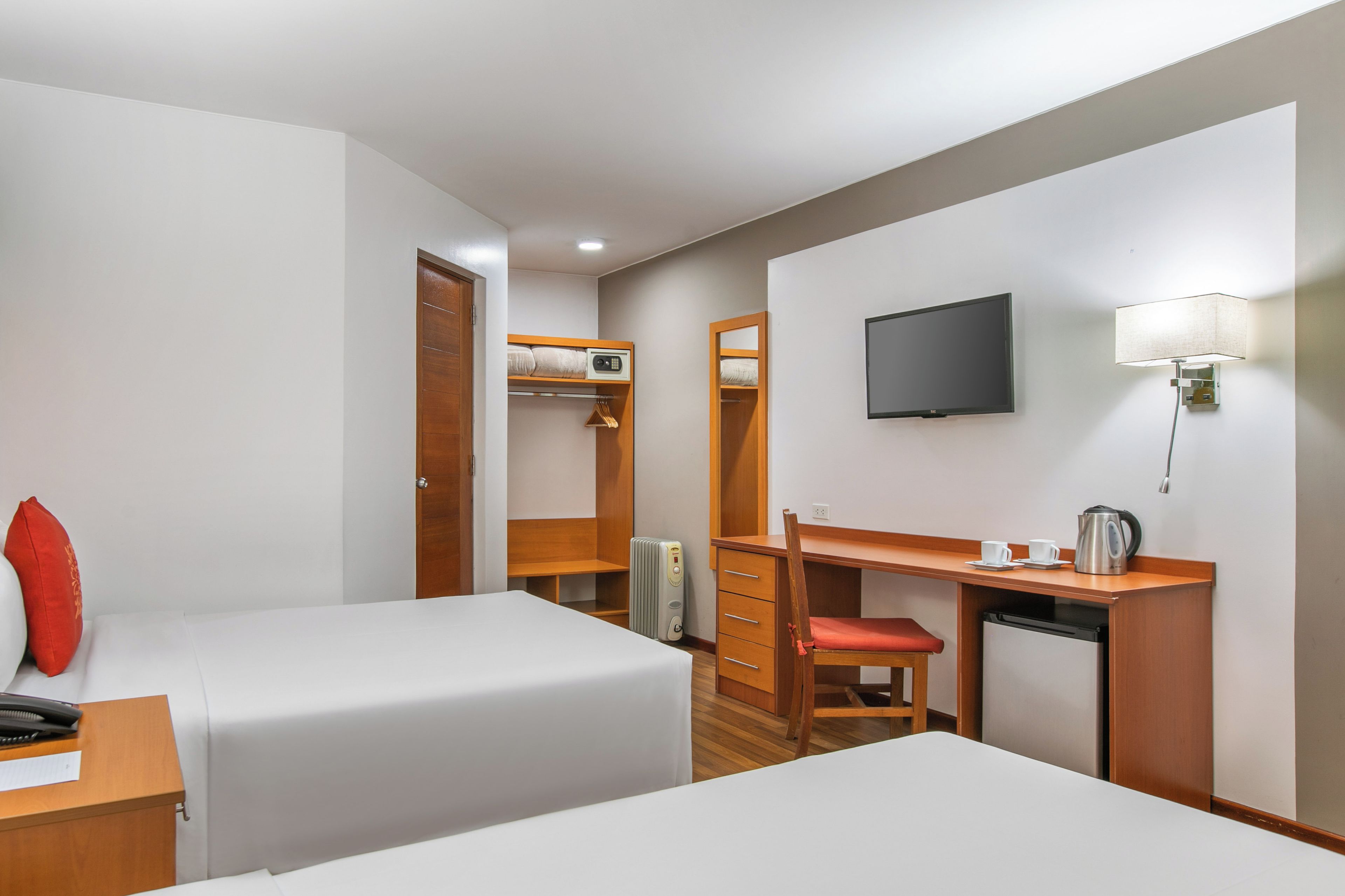 A hotel room with two beds, a desk with a chair, a television, a lamp, and a heater.