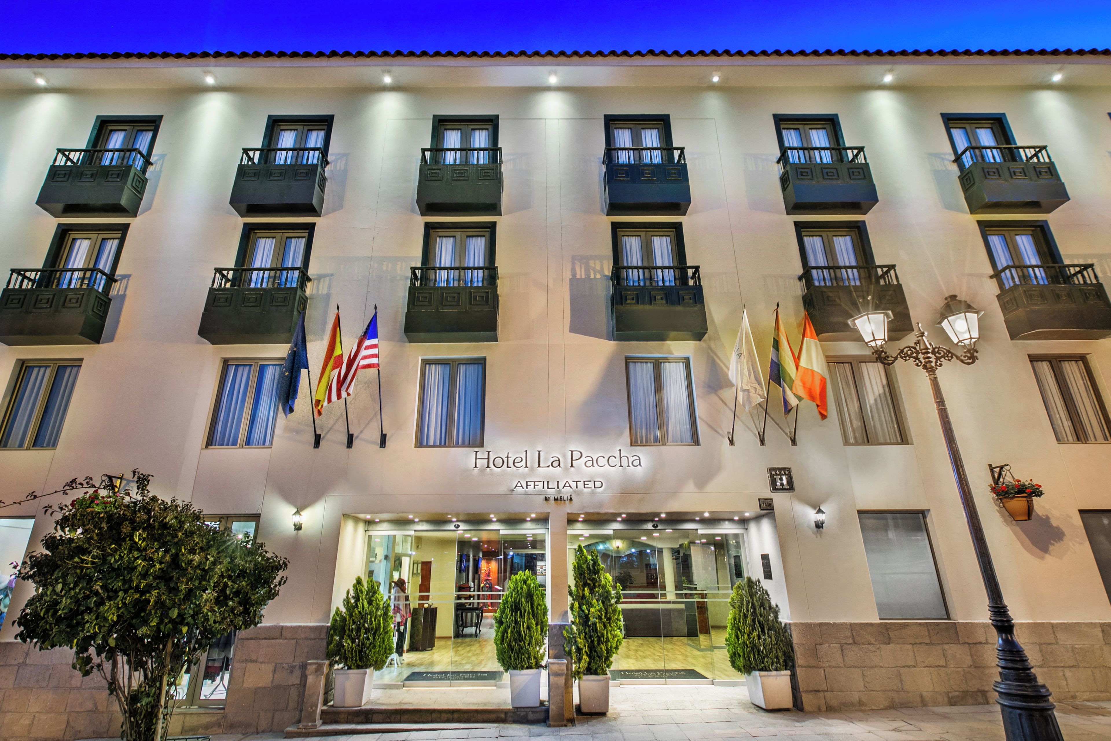Fachada de hotel con varios balcones, banderas y una entrada bien iluminada.