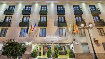 Fachada de hotel con varios balcones, banderas y una entrada bien iluminada.