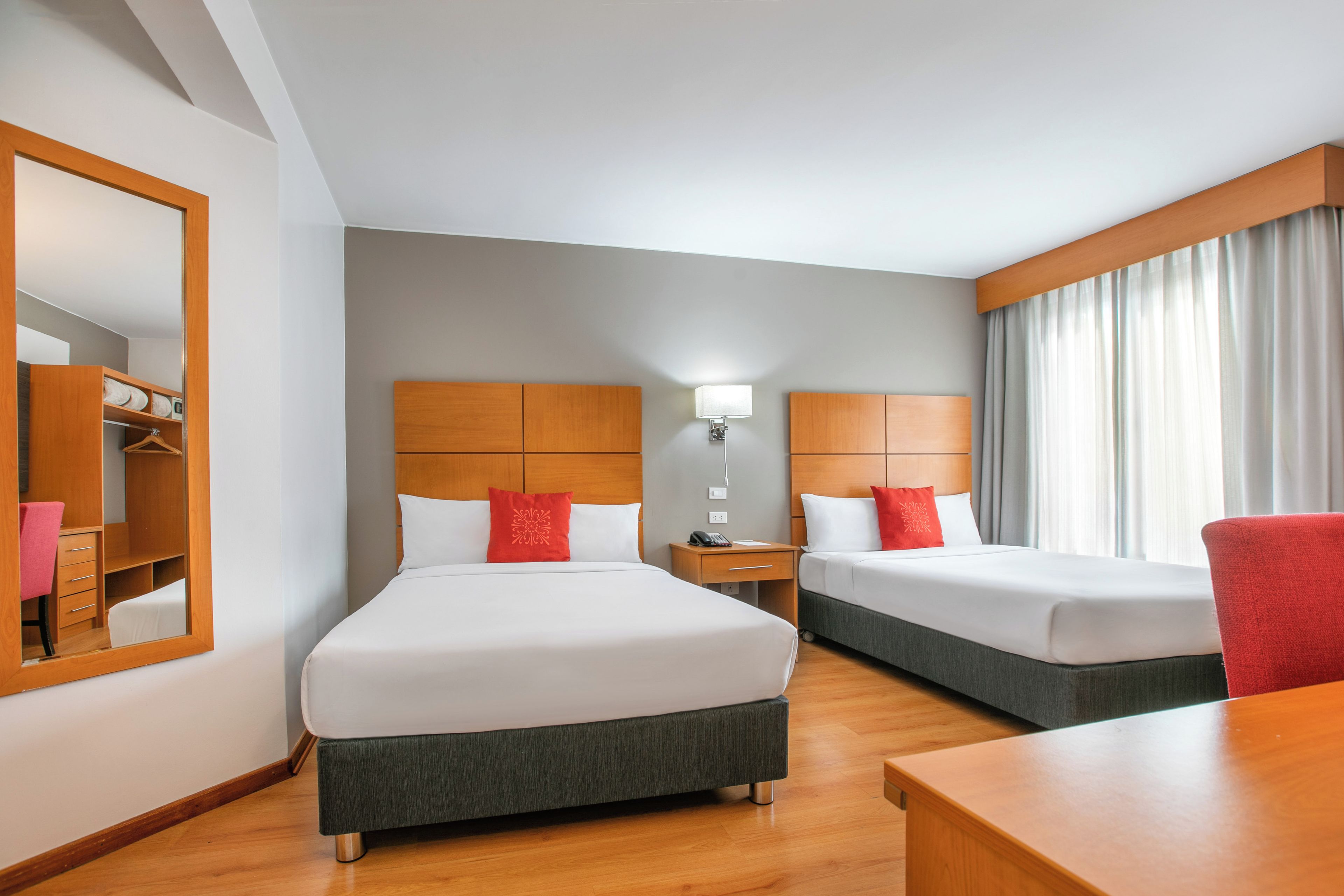Una habitación de hotel con dos camas, un armario, un escritorio y un espejo.