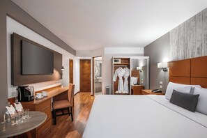 Quarto de hotel com cama, escrivaninha com cafeteira, cadeira, armário e banheiro com espelho e roupão.