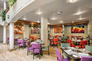 Un restaurante moderno con varias zonas de comedor, arte colorido en las paredes y diversas opciones de asientos.