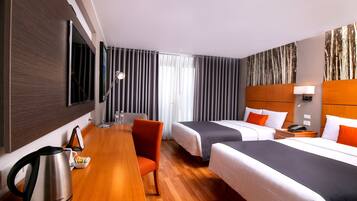 Habitación de hotel con dos camas, un escritorio de madera, un hervidor y una silla.