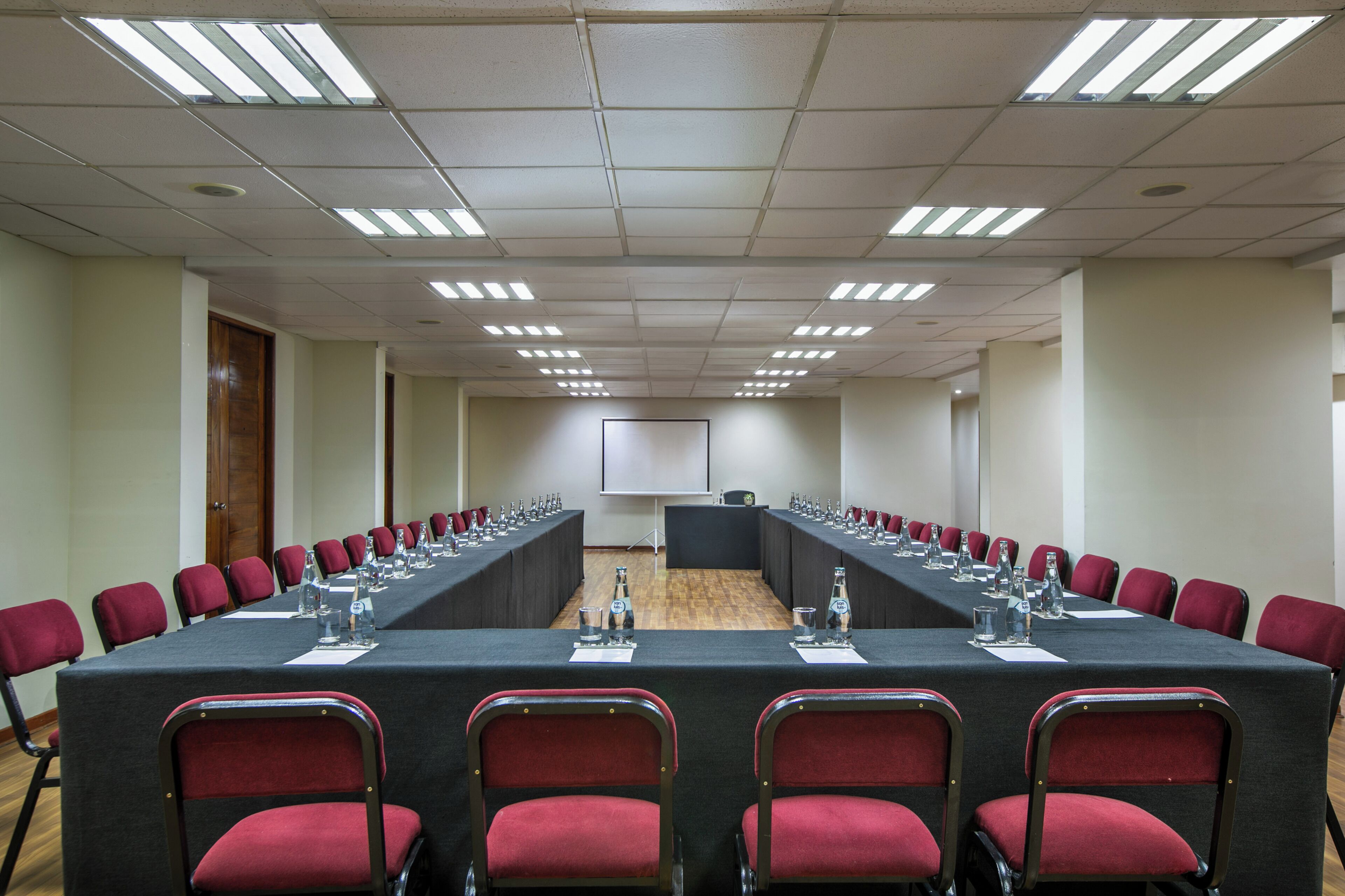 Une salle de conférence avec une longue table, des chaises rouges et un écran de projection à l’avant.