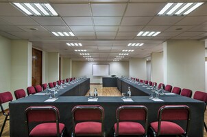 Un salón de conferencias con una larga mesa, sillas rojas y una pantalla de proyector al frente.