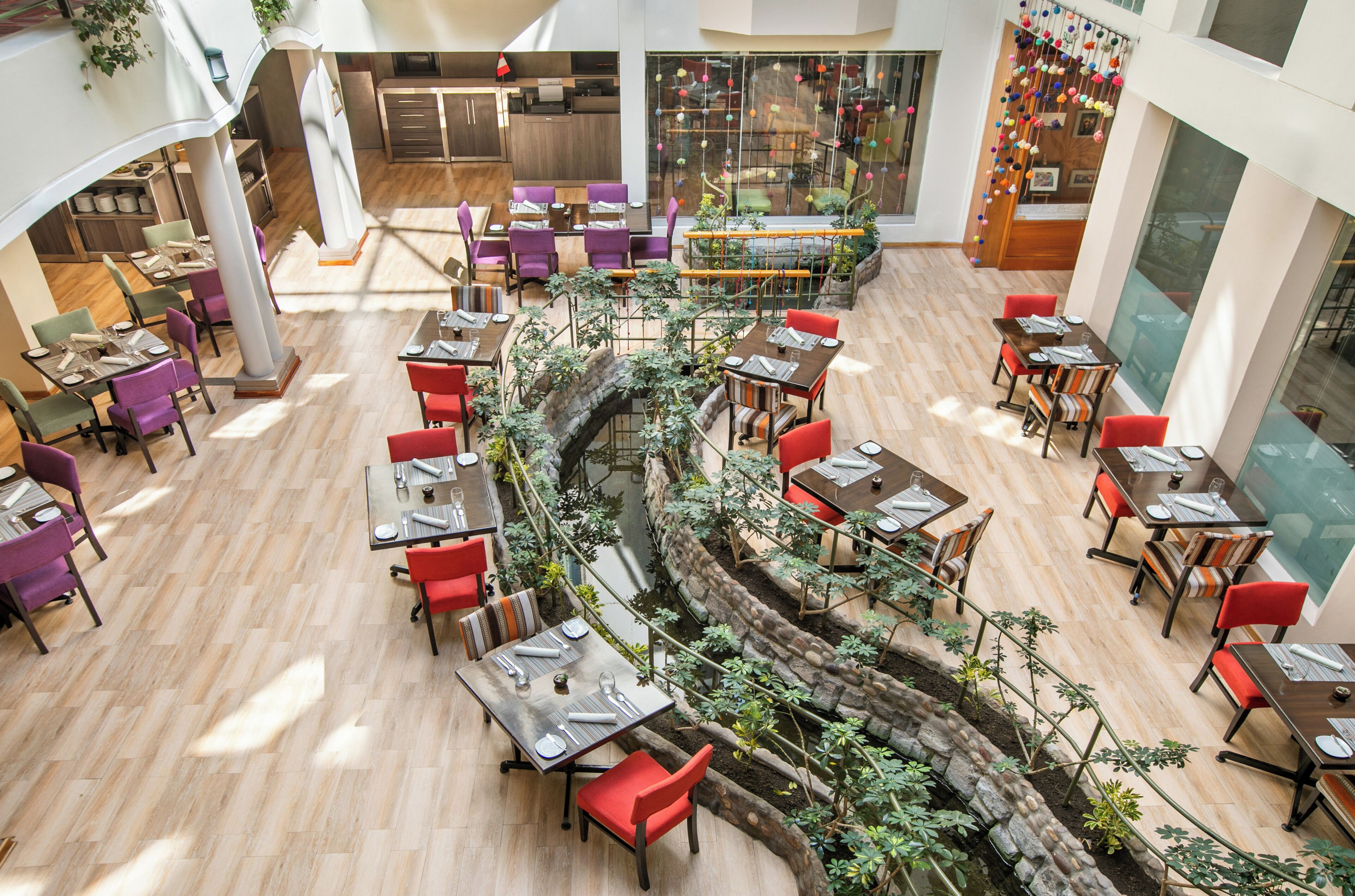 Un área de comedor de varios niveles con mesas y sillas, una fuente central y vistas al área de cocina y comedor al fondo.