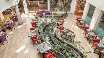 Un área de comedor de varios niveles con mesas y sillas, una fuente central y vistas al área de cocina y comedor al fondo.