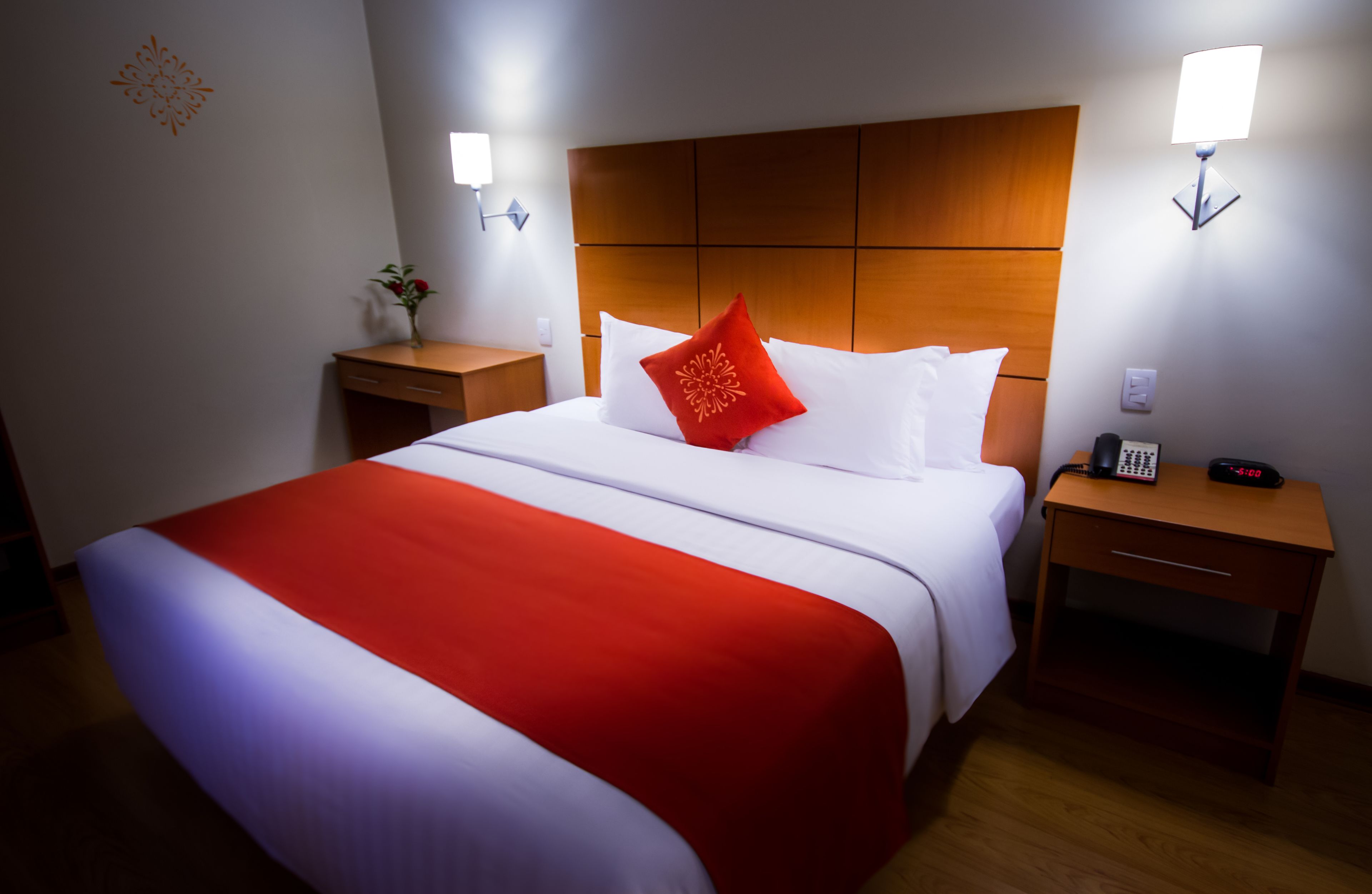A hotel room with a large bed, a wooden headboard, bedside tables, and a nightstand with a clock.