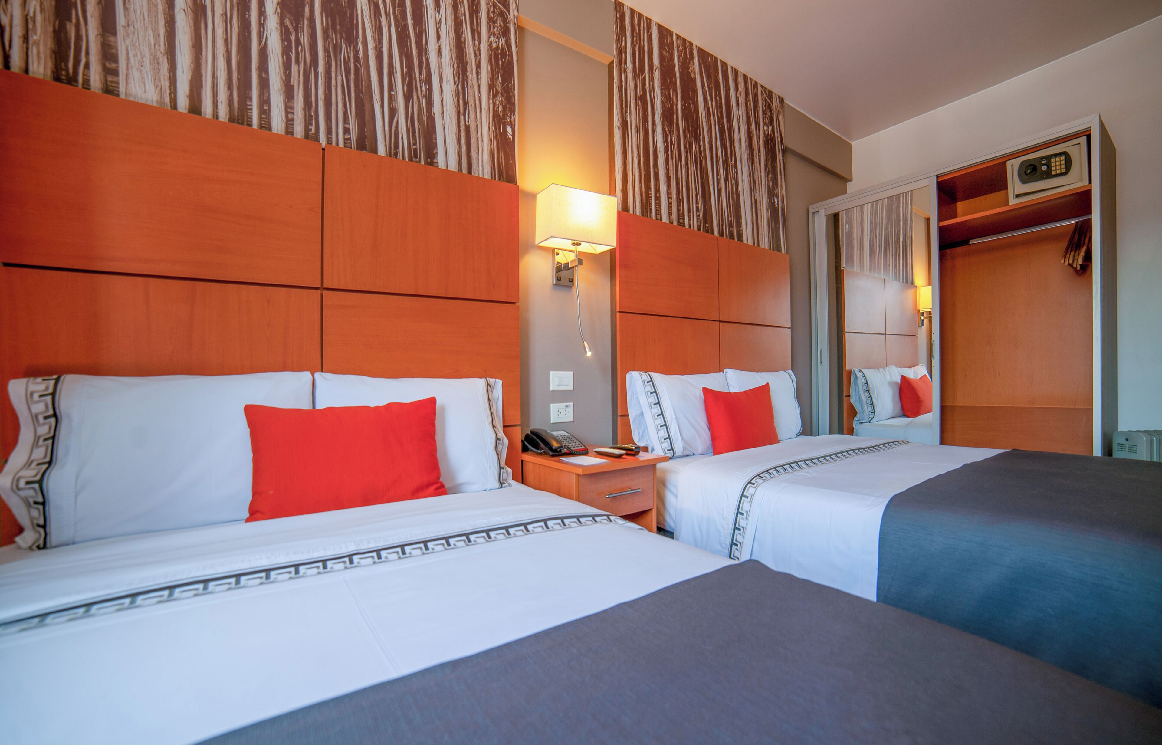A hotel room with two beds, each with white bedding and red pillows, a nightstand with a phone, and a mirror cabinet with a radio.