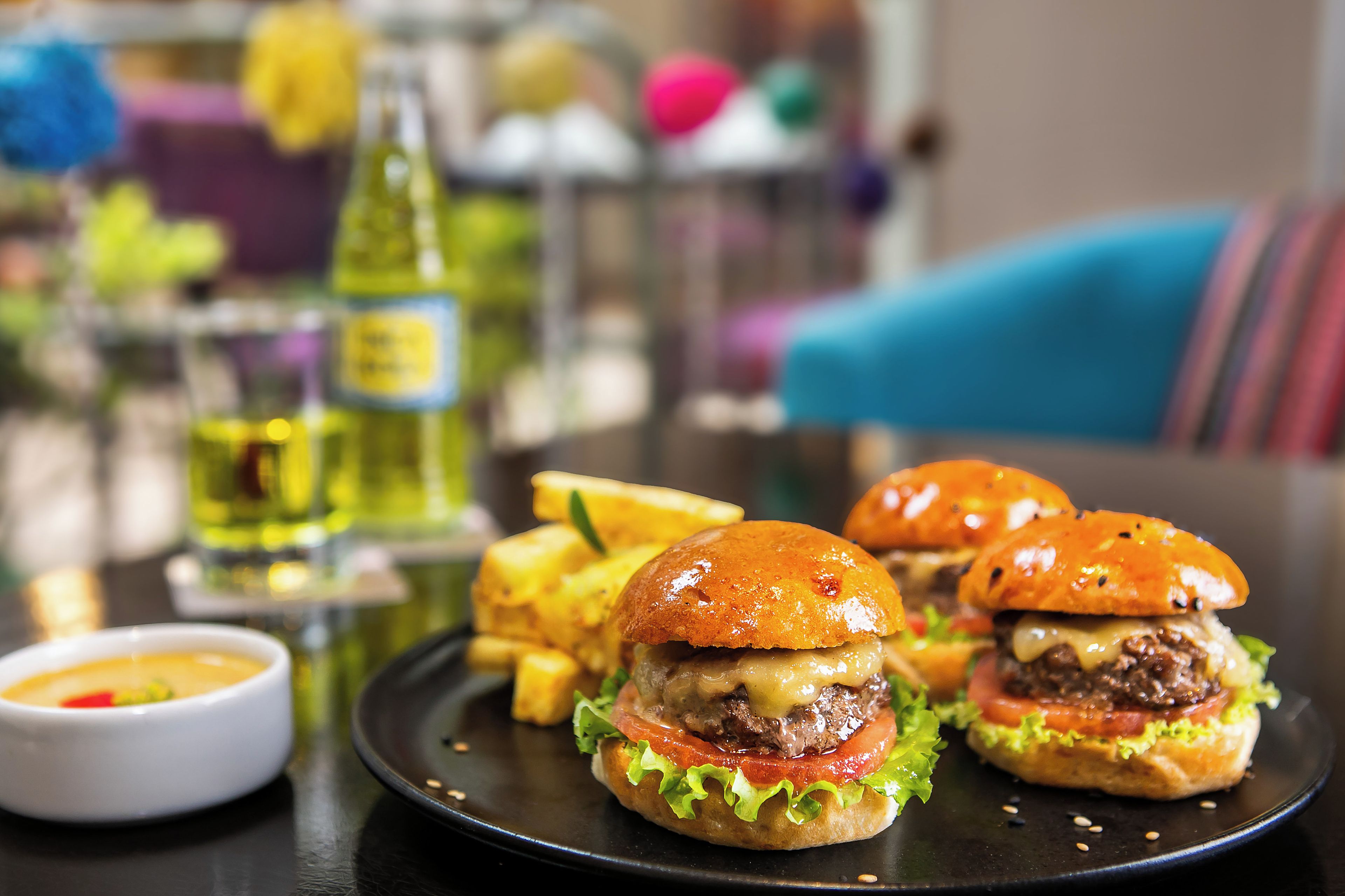 A plate with burgers and fries, a bottle of sauce, and a bowl of dipping sauce on a table.