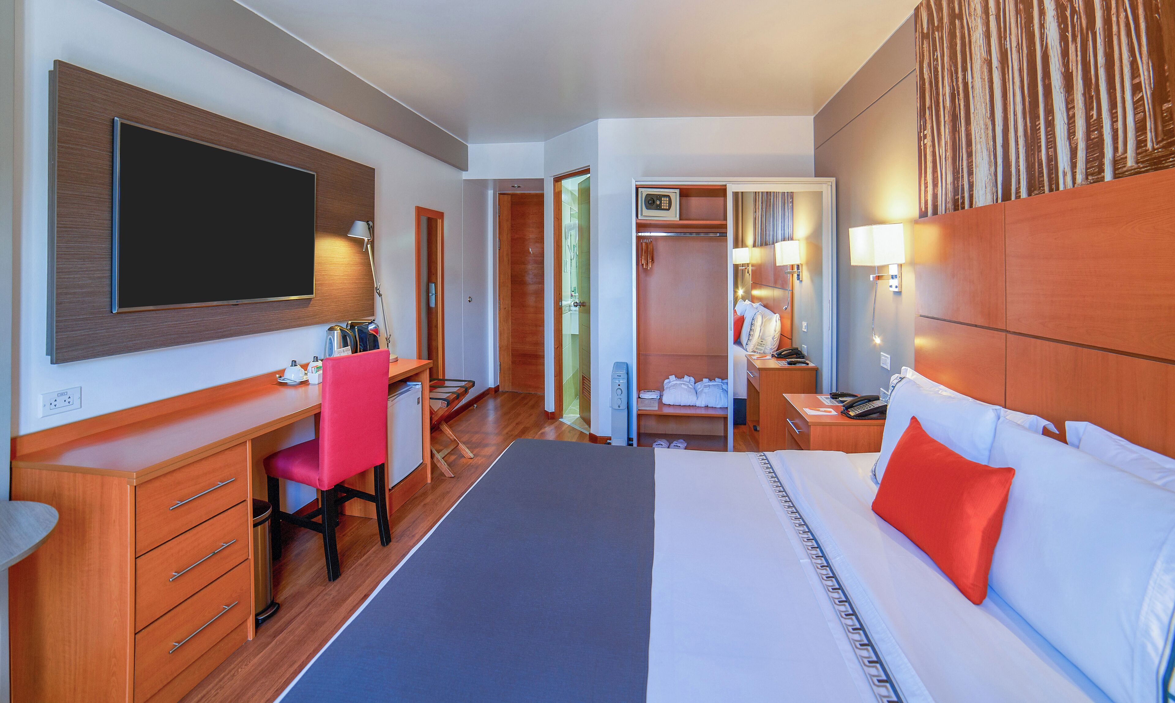 A hotel room with a bed, desk, chair, wardrobe, and a television.