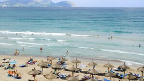 Una playa con sombrillas de paja y tumbonas, vista despejada al mar y montañas en la distancia.