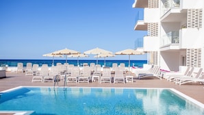 Zona junto a la piscina con sillas de descanso y sombrillas, con vistas al mar.