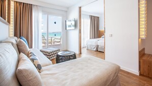Habitación de hotel con cama, una mesita redonda, un sofá y vista al mar a través de un ventanal grande.