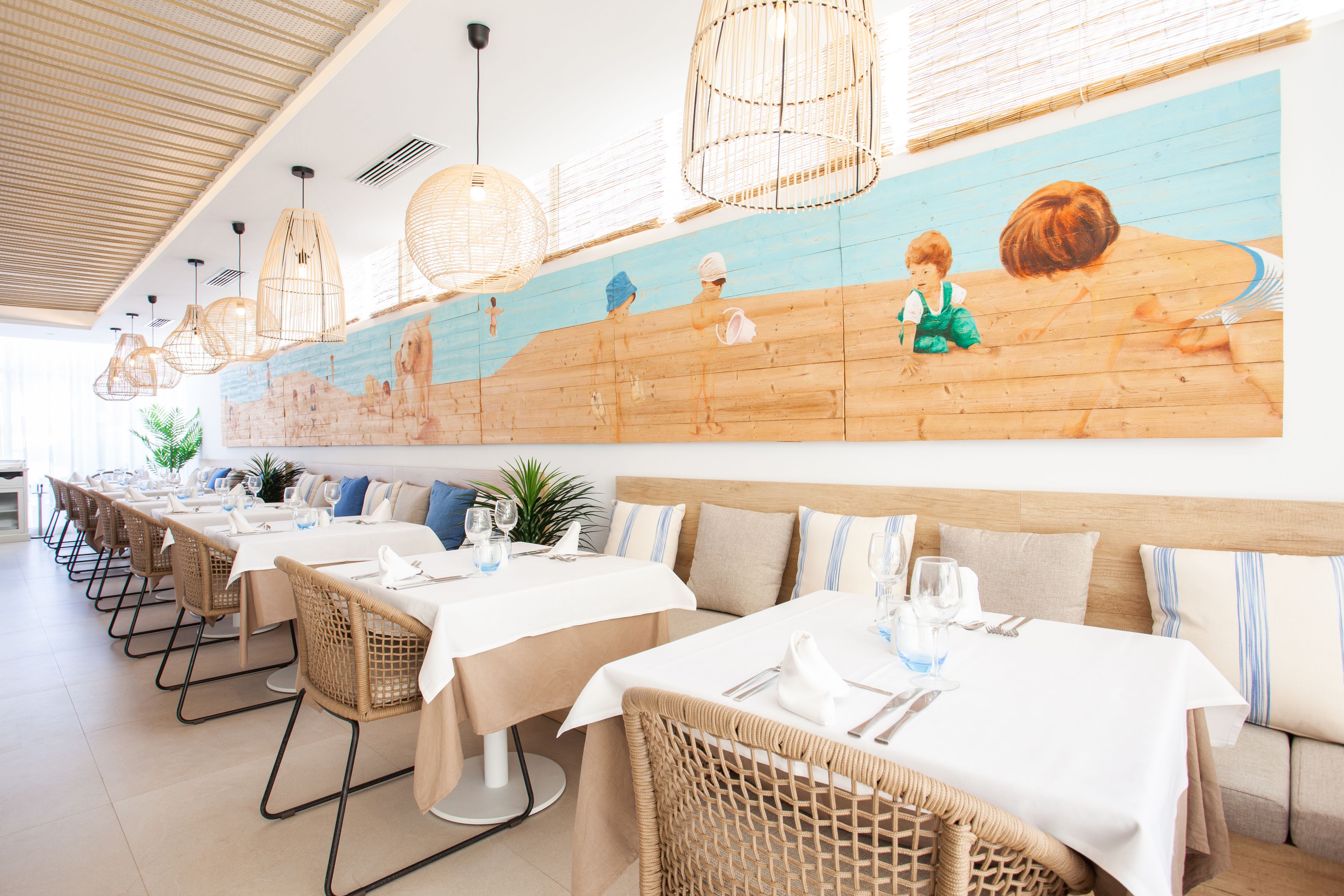 Un espace repas avec de longues tables, des chaises en osier et des luminaires suspendus.