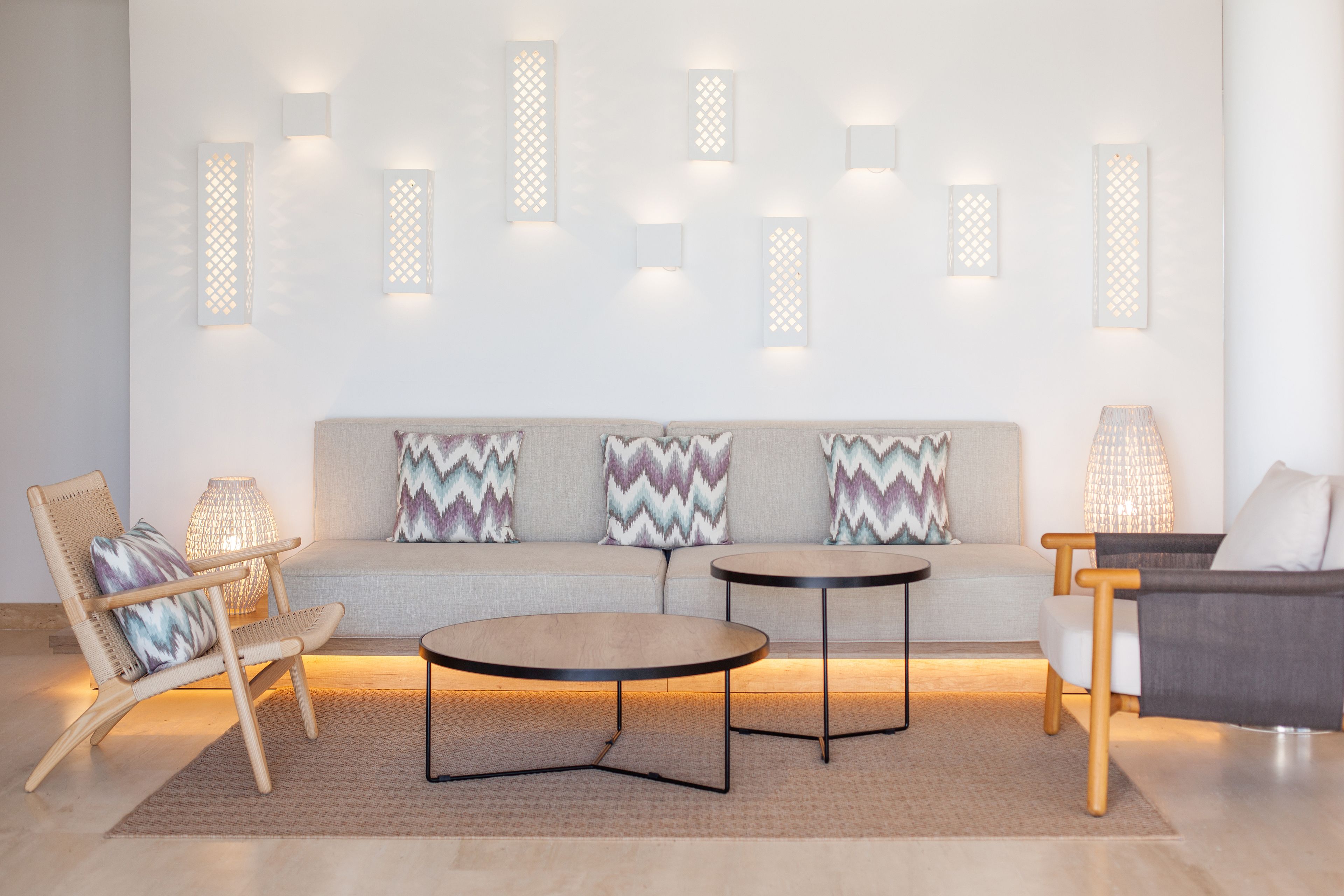 A modern living room with a sofa, two round tables, a wicker chair, and decorative wall sconces.