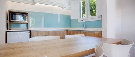 Une cuisine moderne avec une table en bois et des chaises blanches, un four encastré et une fenêtre donnant sur un paysage verdoyant.