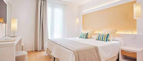 A modern bedroom with a large bed, bedside tables, a nightstand, a mirror, and a window with curtains.