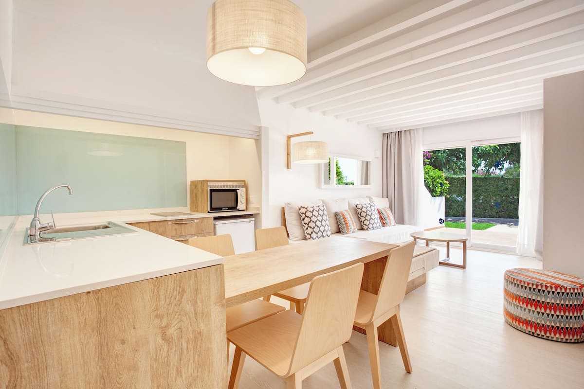 Une cuisine moderne dotée d’un grand îlot central, d’un coin repas avec une table et des chaises en bois, et offrant une vue sur le jardin par la fenêtre.