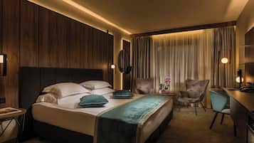A hotel room with a bed, two chairs, a desk, and a large window with curtains.