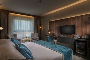 Habitación de hotel con una cama grande, dos sillones, un escritorio, un televisor y un minibar.