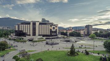 A large public square with a central building, fountains, and surrounding greenery.