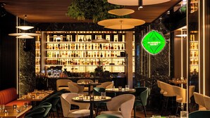 Zona de bar con diversas opciones de asientos, una estantería repleta de licores y un letrero de neón.