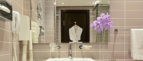 A modern bathroom with a glass sink, a mirror, and a vase with purple flowers.