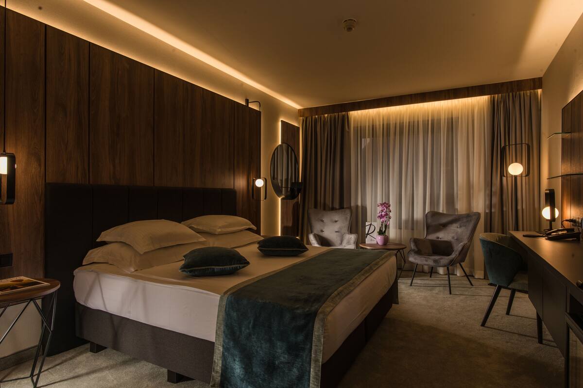 A modern hotel room with a large bed, a desk, two chairs, and a small table.