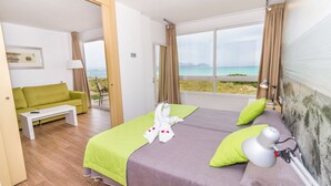 A hotel room with a bed, a green sofa, a small table, and a view of the beach. - Eix Platja Daurada Hotel & Spa (Santa Margalida)
