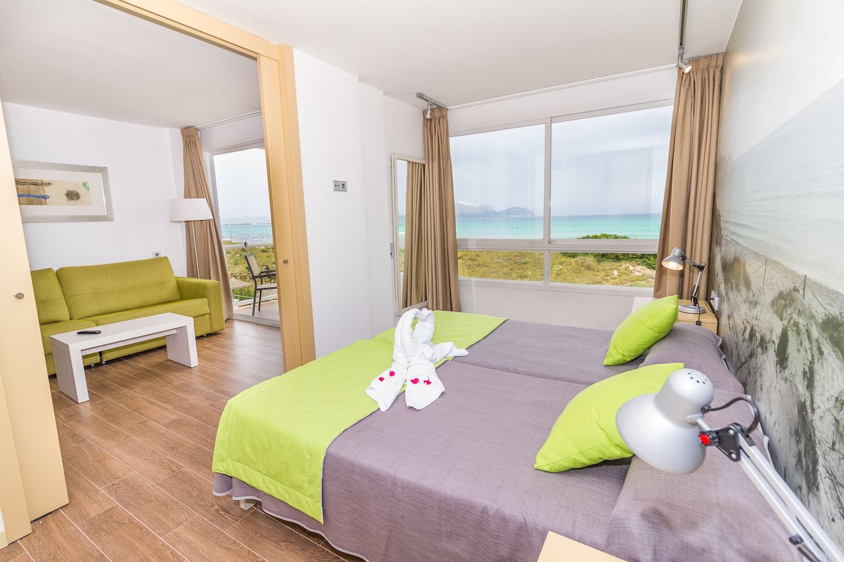 Una habitación de hotel con cama, sofá verde, una mesita y vista a la playa.