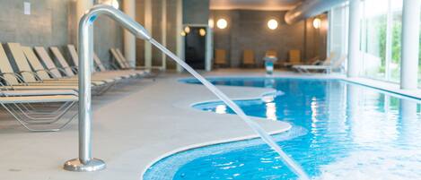 An indoor swimming pool with multiple lanes, lounge chairs, and a modern architectural design.