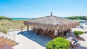 A beachside restaurant with a thatched roof, outdoor seating, and a view of the sea. - Eix Platja Daurada Hotel & Spa (Santa Margalida)