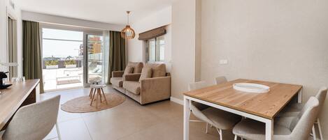 A modern living room with a wooden dining table, beige sofa, and a view of the city through large windows.