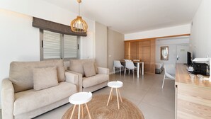 Una sala de estar moderna con un sofá, dos mesas auxiliares, una alfombra tejida y un comedor con sillas y una mesa.