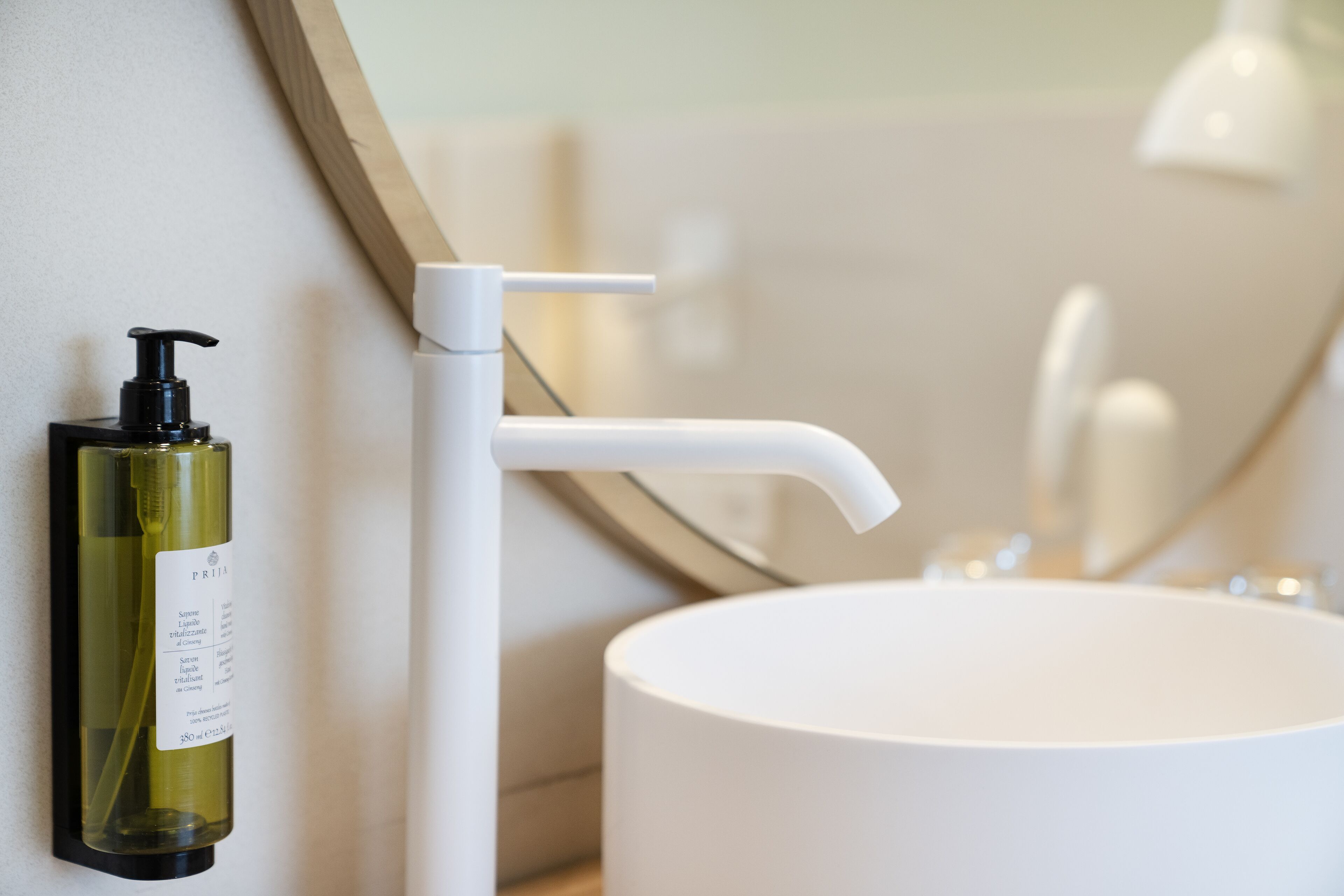 Un baño con un lavamanos blanco, una botella de jabón líquido y un espejo.