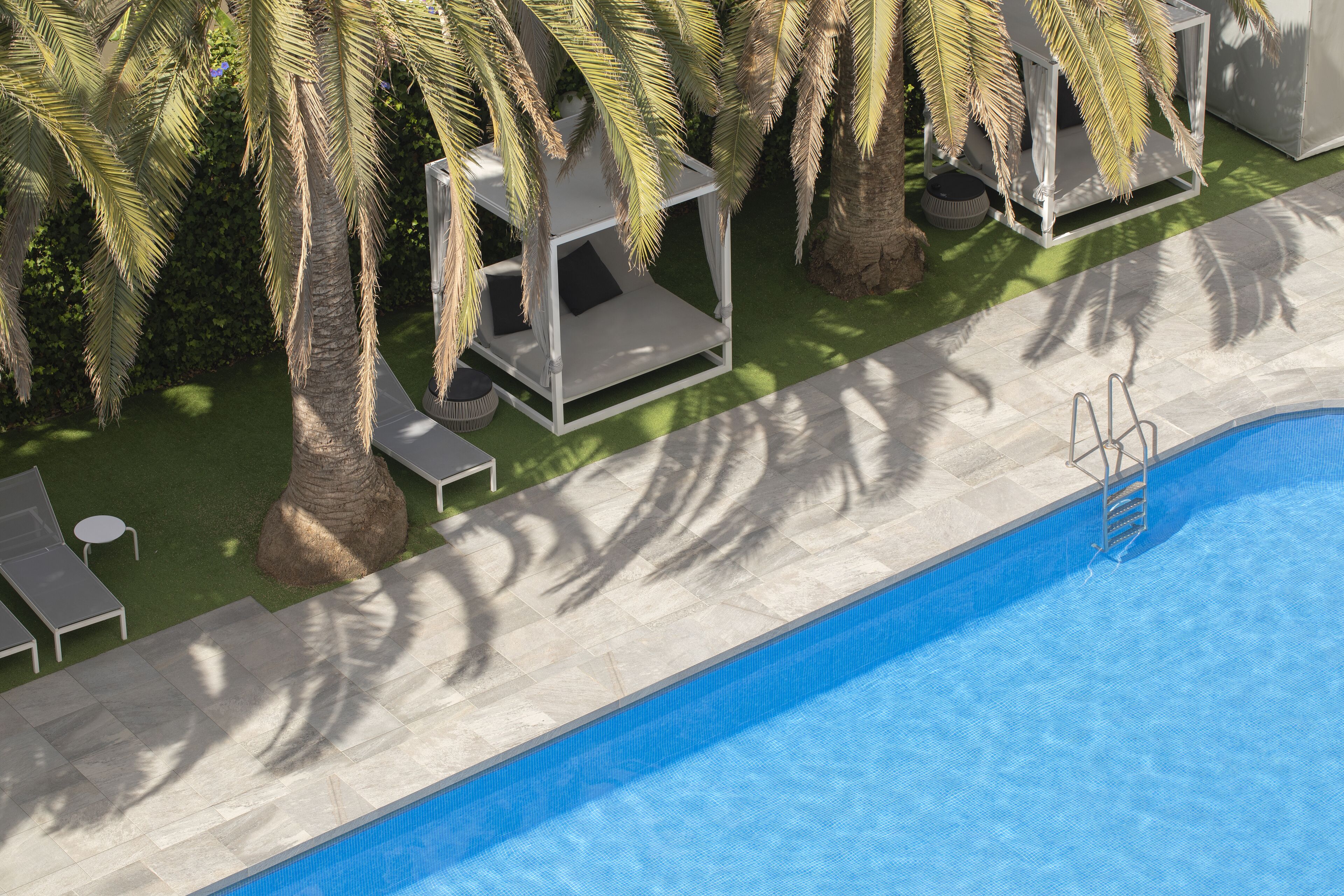 A swimming pool with a white deck, palm trees, and lounge chairs.