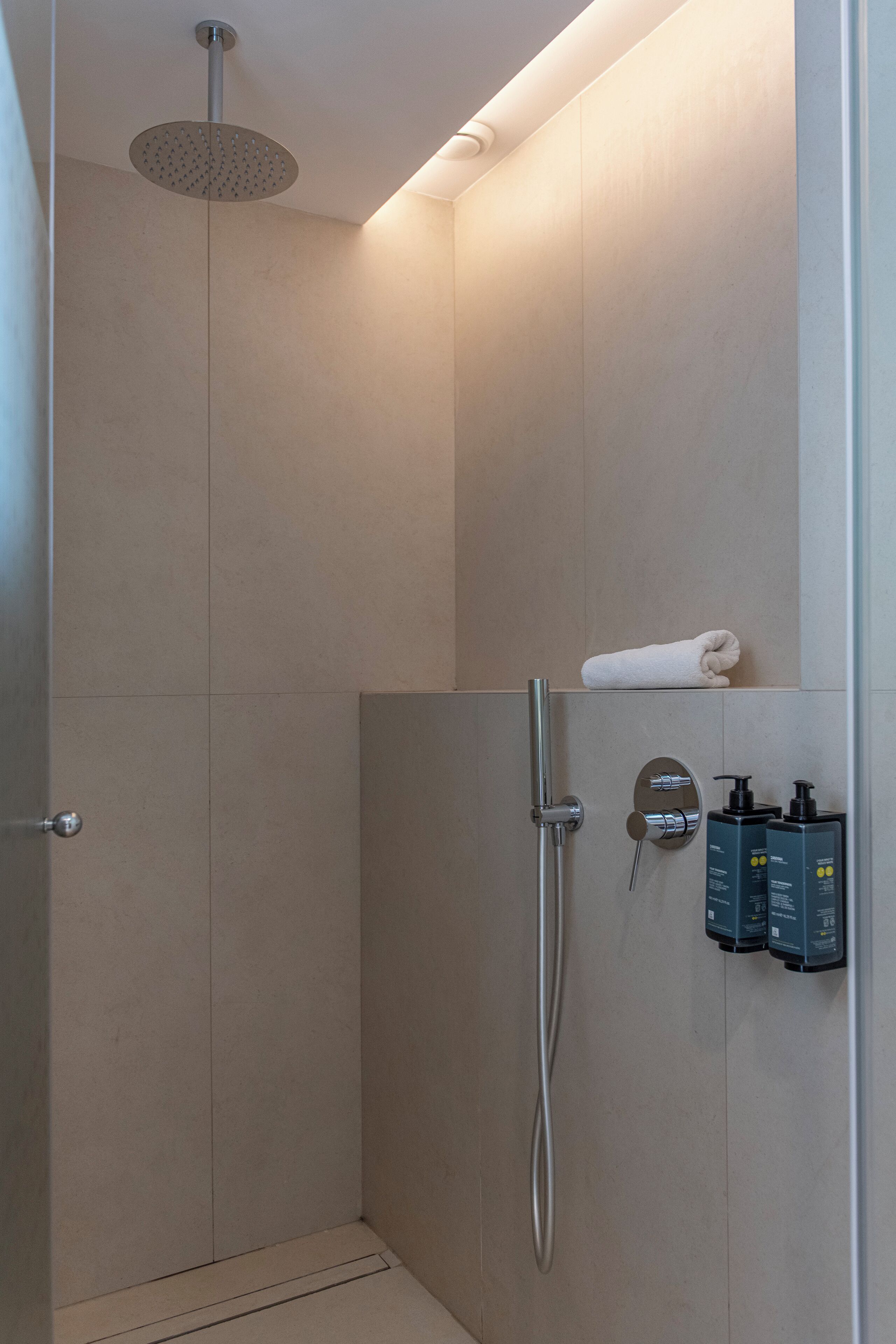 A modern shower area with a handheld showerhead, a wall-mounted towel rack, and two bottles of toiletries.