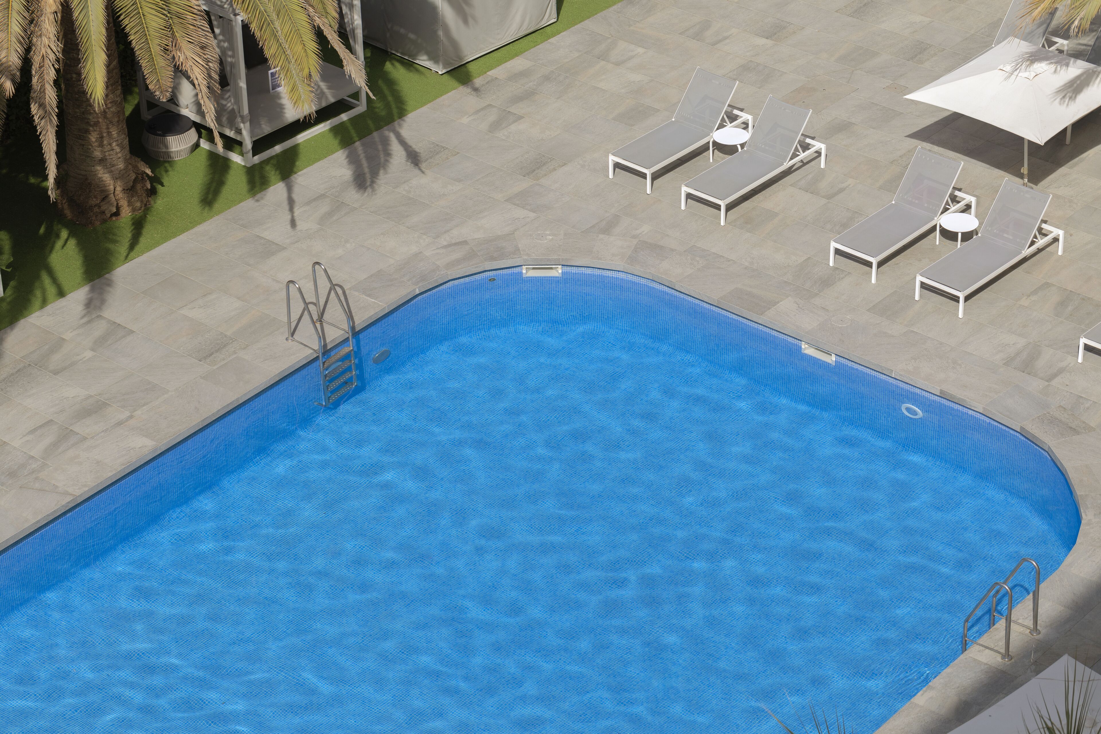 Una piscina rectangular con una escalera en un lateral, rodeada de sillas de descanso y sombrillas.